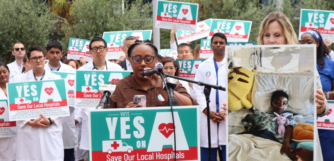 A woman speaks at a podium with a crowd of people behind her holding signs