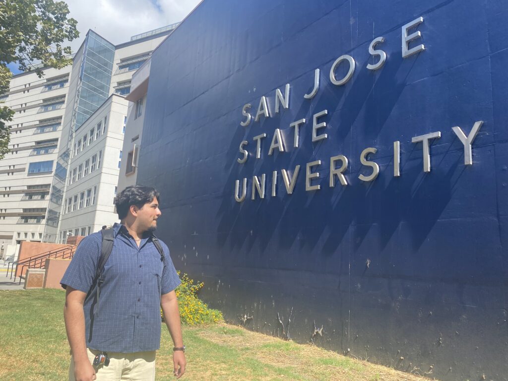 A student stands in front of a sign at San Jose State University