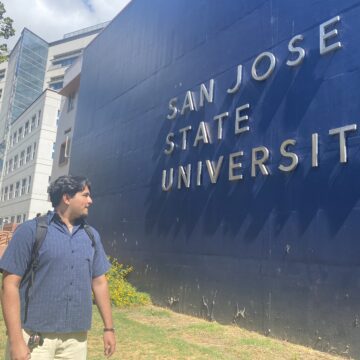 A student stands in front of a sign at San Jose State University