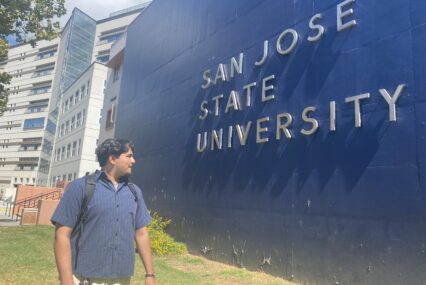 A student stands in front of a sign at San Jose State University