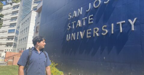 A student stands in front of a sign at San Jose State University