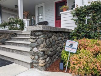 A sign sticks out of the ground in a resident's front yard that reads, "Warning! Protected by Surveillance Solutions alarm system."