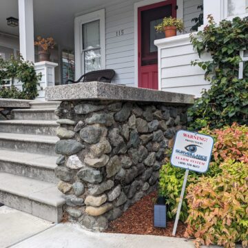 A sign sticks out of the ground in a resident's front yard that reads, "Warning! Protected by Surveillance Solutions alarm system."
