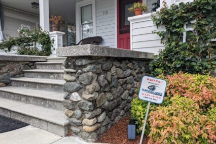 A sign sticks out of the ground in a resident's front yard that reads, "Warning! Protected by Surveillance Solutions alarm system."