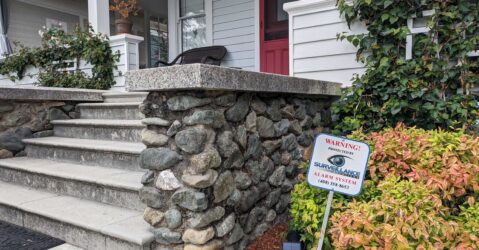 A sign sticks out of the ground in a resident's front yard that reads, "Warning! Protected by Surveillance Solutions alarm system."
