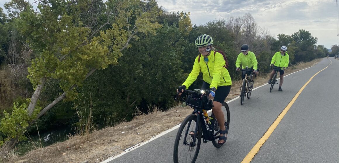 Three people in bright yellow jackets riding bikes outside on a trail in San Jose, California