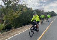 Three people in bright yellow jackets riding bikes outside on a trail in San Jose, California