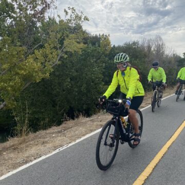Three people in bright yellow jackets riding bikes outside on a trail in San Jose, California