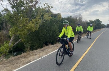 Three people in bright yellow jackets riding bikes outside on a trail in San Jose, California