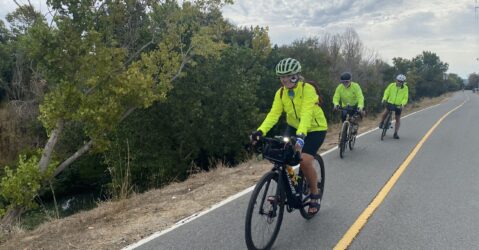 Three people in bright yellow jackets riding bikes outside on a trail in San Jose, California