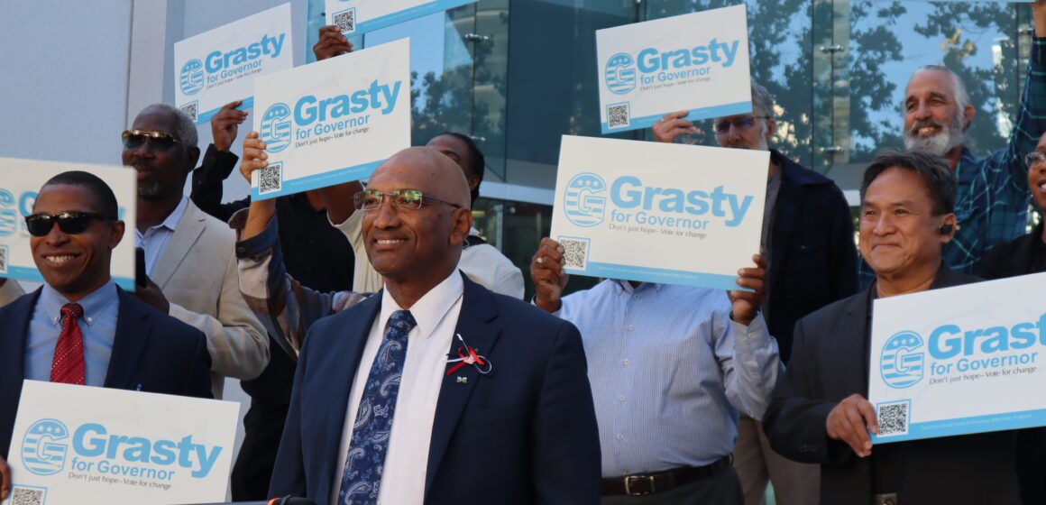 A man stands at a podium with people holding signs behind him