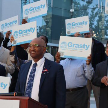 A man stands at a podium with people holding signs behind him