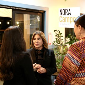 A woman facing the camera speaks to two other women with their backs to the camera