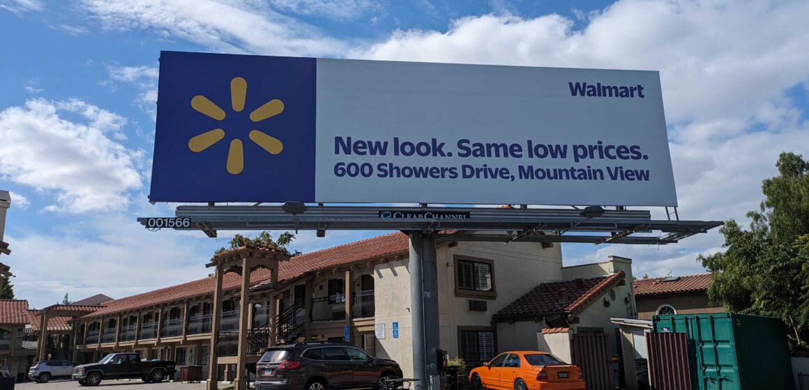 A billboard in front of a hotel with a Walmart ad on it that reads, "New look. Same low prices. 600 Showers Drive, Mountain View."
