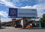 A billboard in front of a hotel with a Walmart ad on it that reads, "New look. Same low prices. 600 Showers Drive, Mountain View."