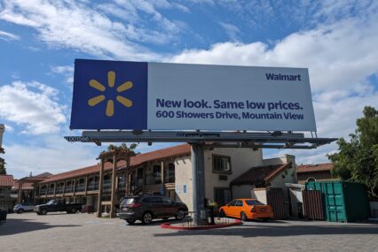 A billboard in front of a hotel with a Walmart ad on it that reads, "New look. Same low prices. 600 Showers Drive, Mountain View."