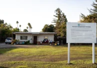 A sign on a green lawn in front of a house