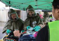 Two people in hazmat suits practice evaluating a medical mannequin