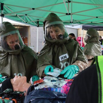 Two people in hazmat suits practice evaluating a medical mannequin