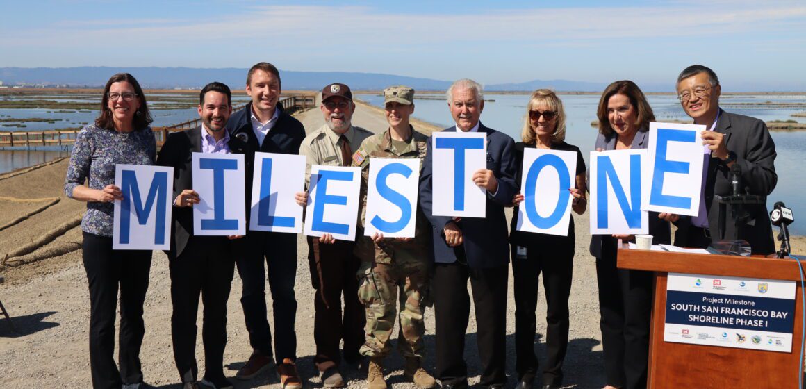 A group of people standing in a row outside holding signs that spell out 'milestone'
