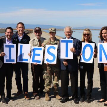 A group of people standing in a row outside holding signs that spell out 'milestone'