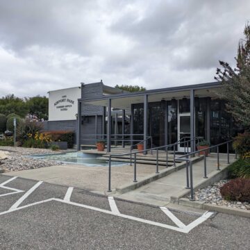 The front of a grey and white building with a sign that reads "Airport Park Garden Office Suites"