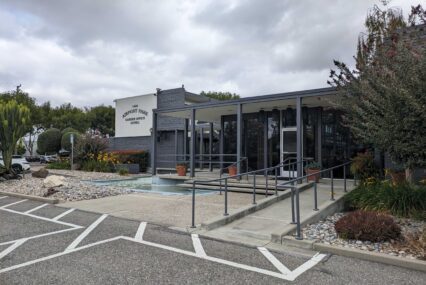 The front of a grey and white building with a sign that reads "Airport Park Garden Office Suites"