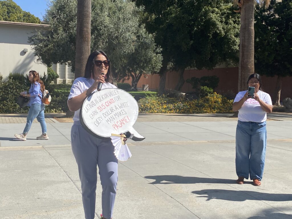 A woman stands outside holding a sign
