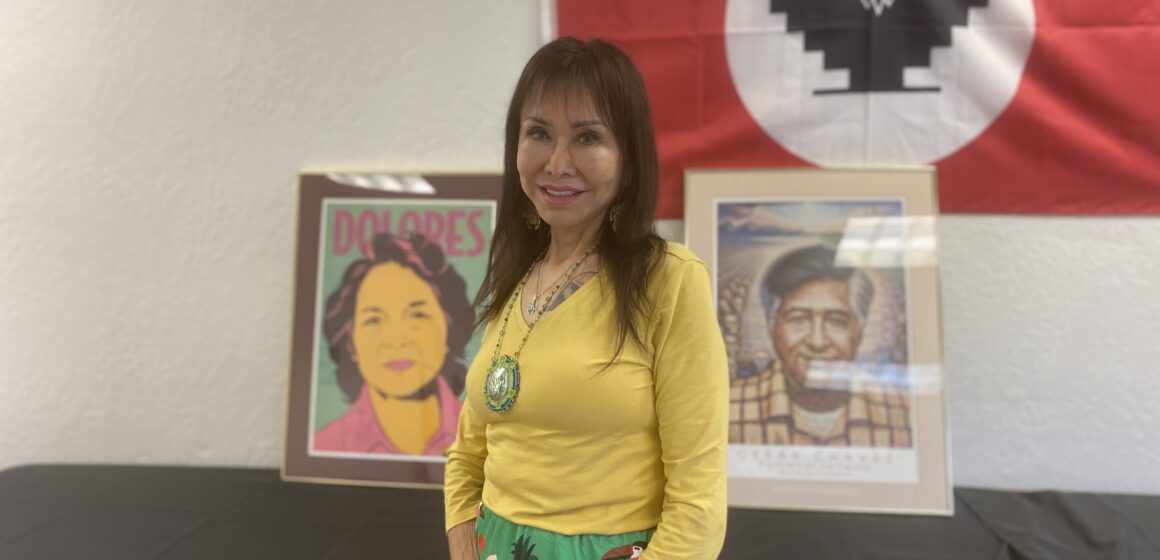 A woman stands in front of a United Farm Workers flag and art depicting civil rights leaders Dolores Huerta and Cesar Chavez.