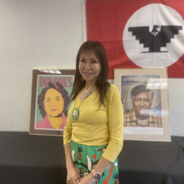 Rose Amador ConXión to Community A woman stands in front of a United Farm Workers flag and art depicting civil rights leaders Dolores Huerta and Cesar Chavez.