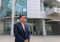 An older man in a suit jacket looks into the distance in front of a big, silver rotunda