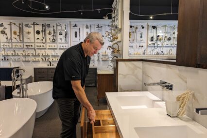 A middle-aged man pulls open a drawer on a display bathroom sink