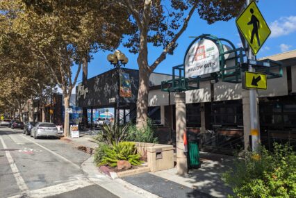 A view down a shady, small downtown street with a crosswalk and a sign that reads "Downtown Willow Glen"