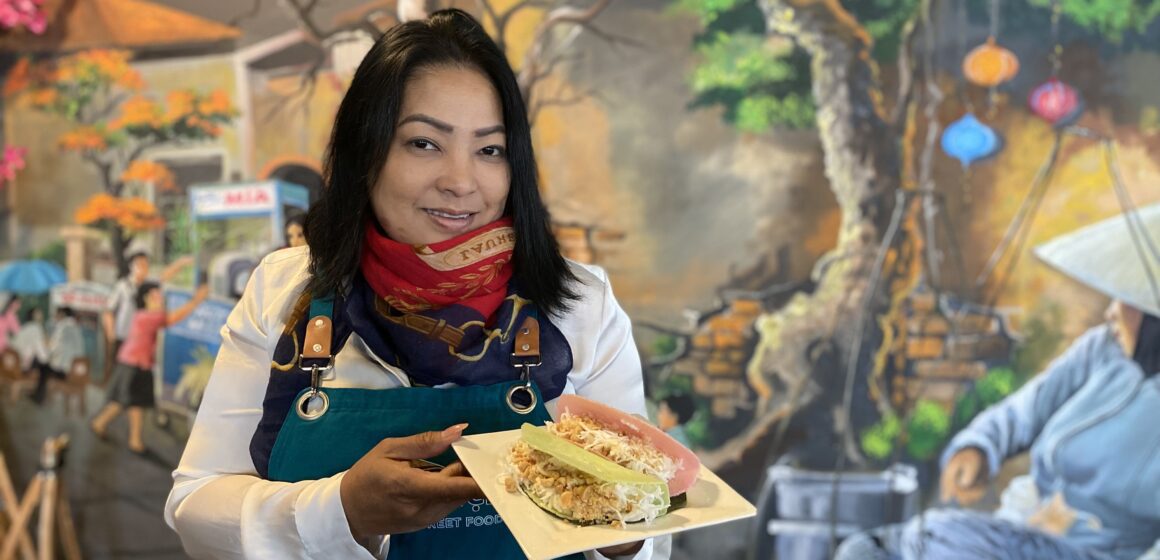A woman in an apron and scarf holds a plate of food inside a restaurant