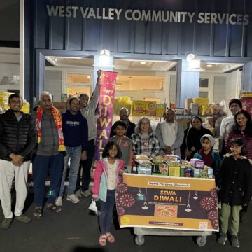 A group of children and adults stand in front of West Valley Community Services surrounded by groceries