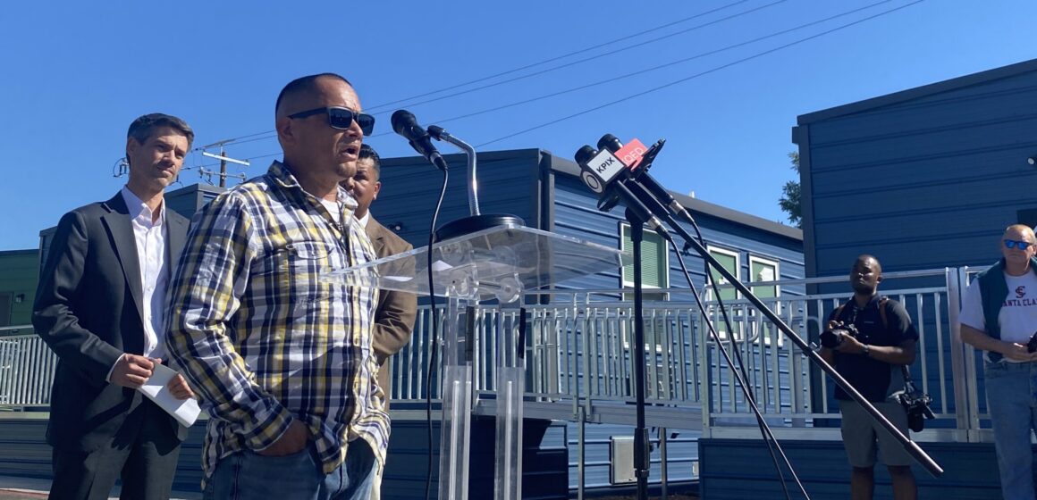 RUE FERRARI EXPANSION A man stands outside speaking into a microphone at a podium in San Jose, California