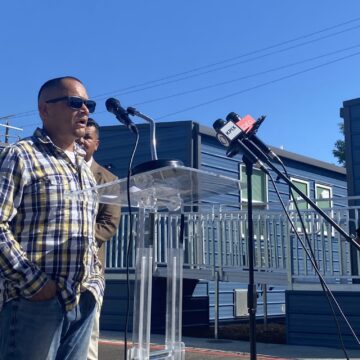 A man stands outside speaking into a microphone at a podium in San Jose, California