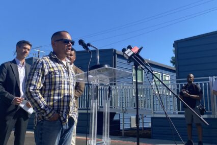 A man stands outside speaking into a microphone at a podium in San Jose, California