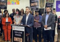 A man in a suit stands at a podium in front of a group of people.