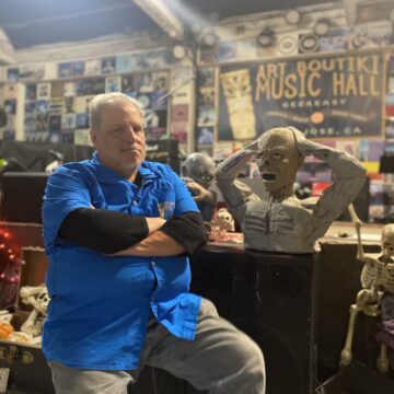 THE ART BOUTIKI A man in a blue shirt standing inside a live music venue in San Jose, California