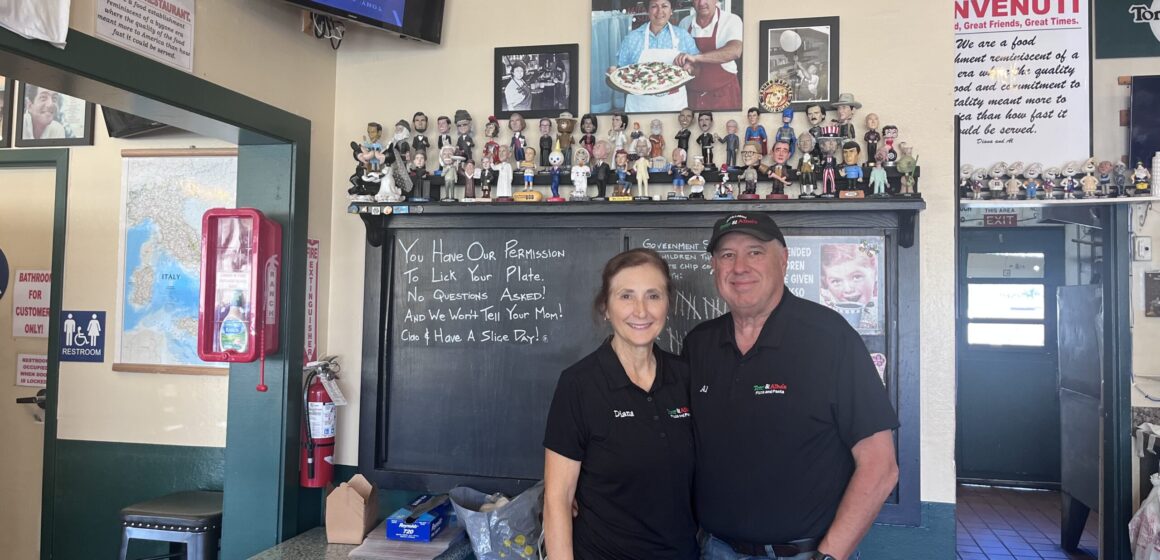 A man and a woman stand in front of a chalk board inside a pizza restaurant in San Jose, California