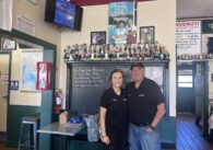 A man and a woman stand in front of a chalk board inside a pizza restaurant in San Jose, California