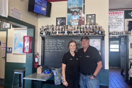 A man and a woman stand in front of a chalk board inside a pizza restaurant in San Jose, California