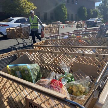 Distribución de alimentos de la Catedral de la Fe Un hombre con chaleco reflectante amarillo arrastra carritos de la compra por un aparcamiento.