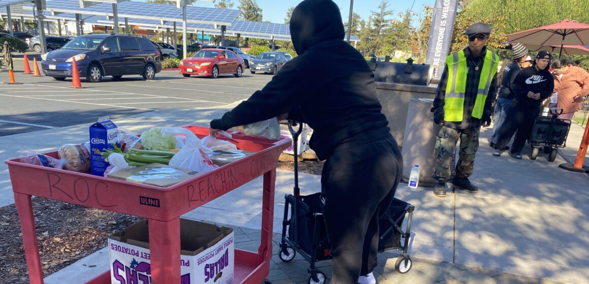 Một người phụ nữ mặc áo nỉ đen đang lấy đồ ăn từ một chiếc ô tô màu đỏ.