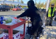 A woman in a black sweatshirt picks up food from a red car.