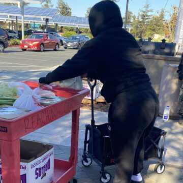 A woman in a black sweatshirt picks up food from a red car.