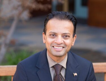 A man in a suit with an American flag pin sitting on a bench