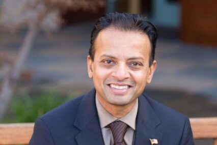 A man in a suit with an American flag pin sitting on a bench