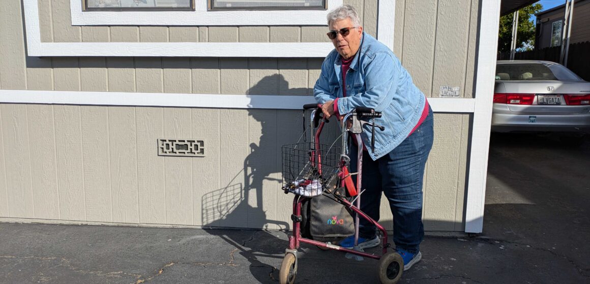GAIL RUBINO -- EL DORADO MOBILE HOME PARK An older woman with short gray hair stands in front of her mobile home, leaning on a walker